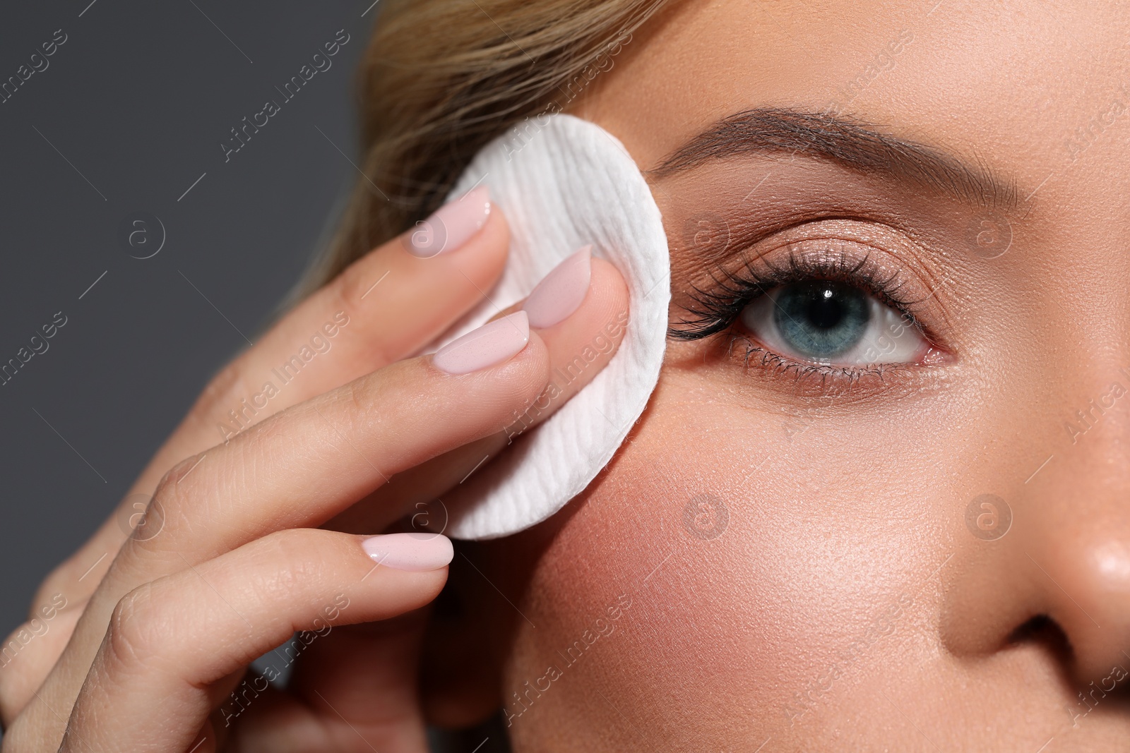 Photo of Beautiful woman removing makeup with cotton pad on dark grey background, closeup