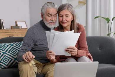 Photo of Elderly couple with papers and laptop discussing pension plan in room