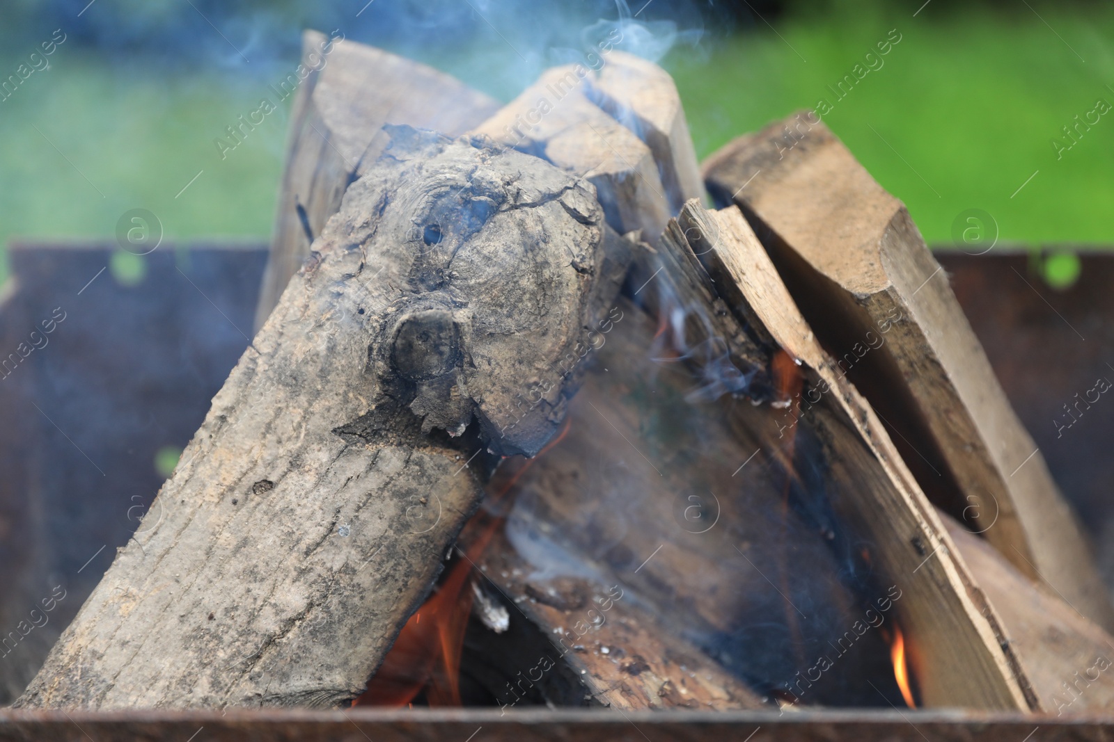 Photo of Metal brazier with burning firewood outdoors, closeup