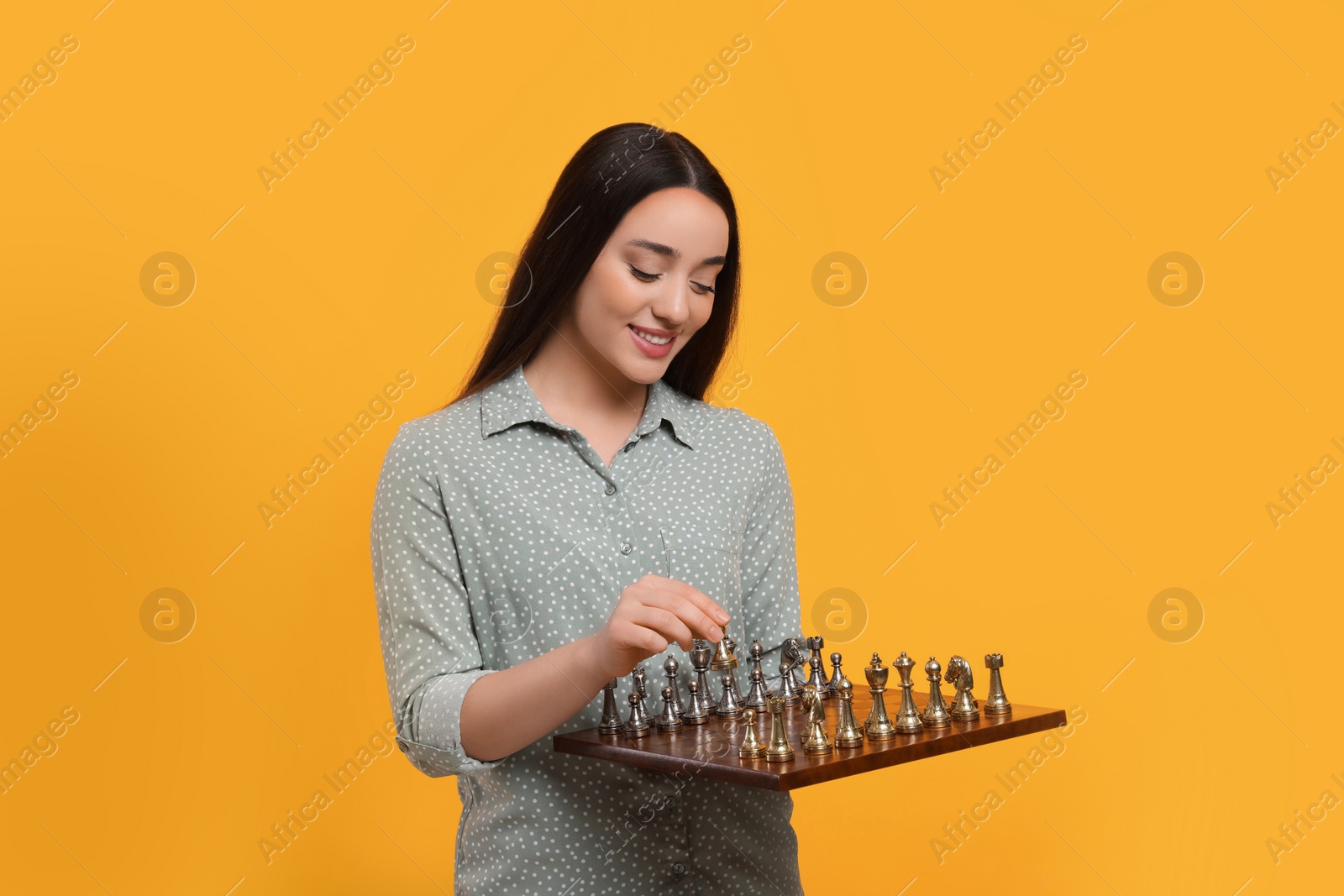 Photo of Happy woman holding chessboard and playing with game pieces on orange background