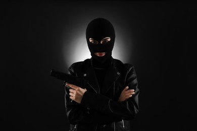 Woman wearing knitted balaclava with gun on black background