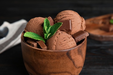 Photo of Wooden bowl of chocolate ice cream and mint on table, closeup