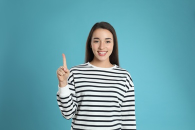 Photo of Woman showing number one with her hand on light blue background