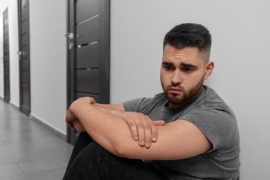 Photo of Sad man sitting on floor in hall. Space for text