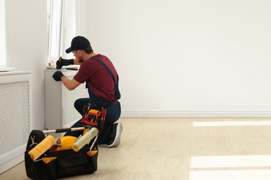 Photo of Handyman in uniform working with screwdriver indoors, space for text. Professional construction tools