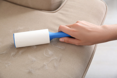 Photo of Woman removing hair from beige sofa, closeup