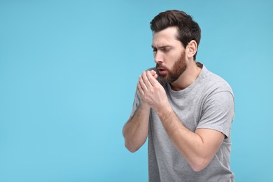 Photo of Sick man coughing on light blue background, space for text. Cold symptoms