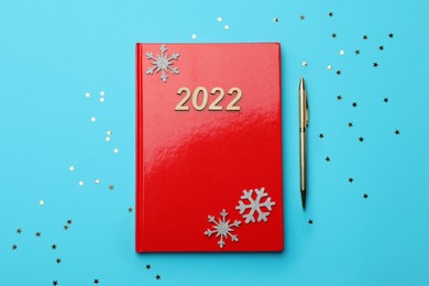 Photo of Red planner, pen, decorative snowflakes and confetti on light blue background, flat lay. Planning for 2022 New Year