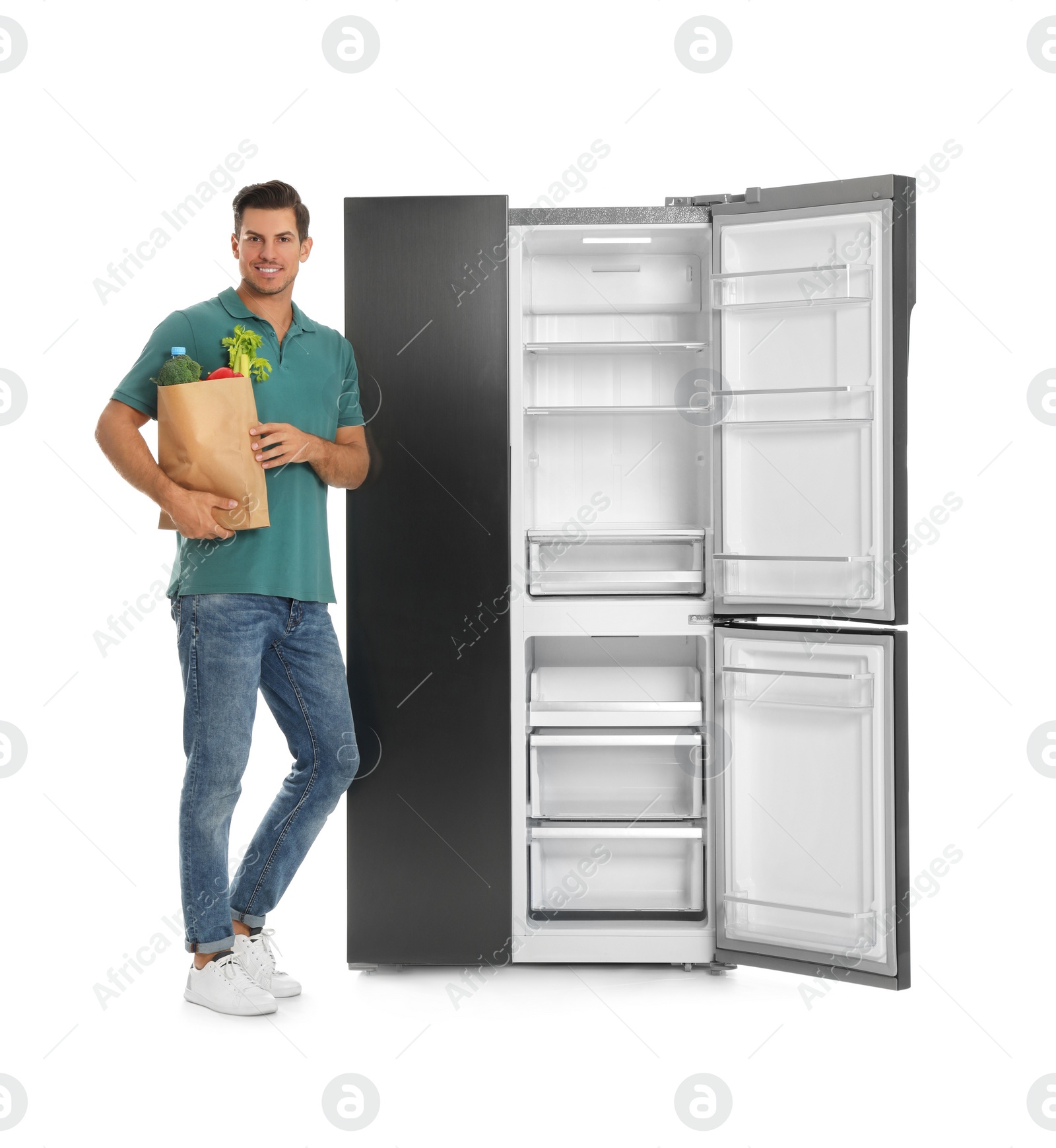 Photo of Man with bag of groceries near open empty refrigerator on white background
