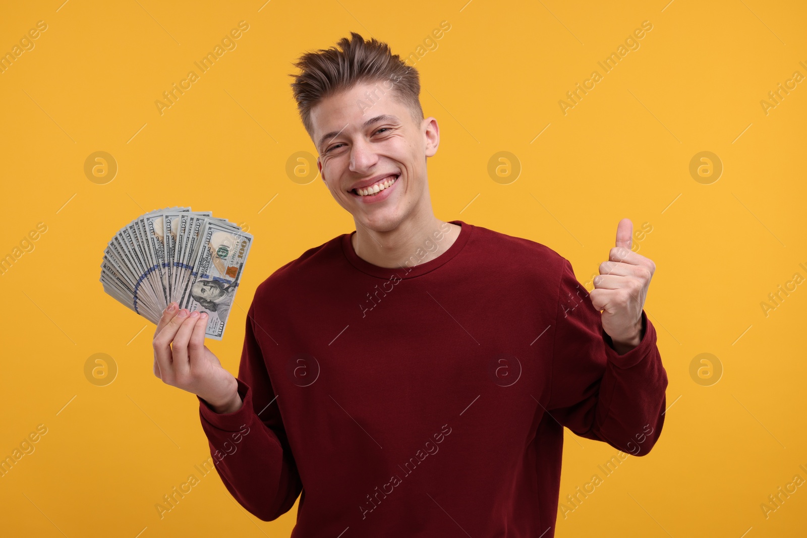 Photo of Happy man with dollar banknotes showing thumb up on yellow background