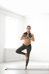 Photo of Young pregnant woman in fitness clothes practicing yoga at home