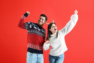 Beautiful happy couple in Christmas headbands and sweaters having fun on red background