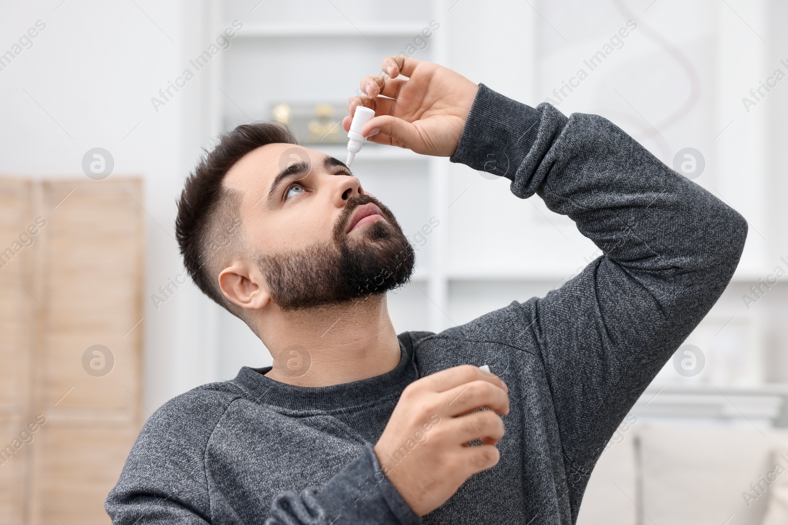 Photo of Young man applying medical eye drops indoors