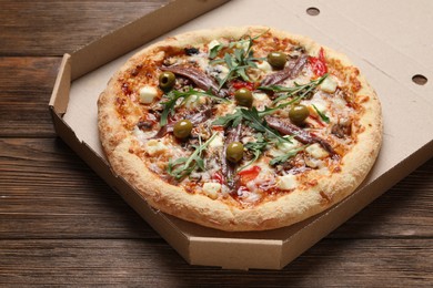 Photo of Tasty pizza with anchovies, arugula and olives on wooden table