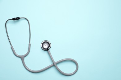 Stethoscope on light blue background, top view. Space for text