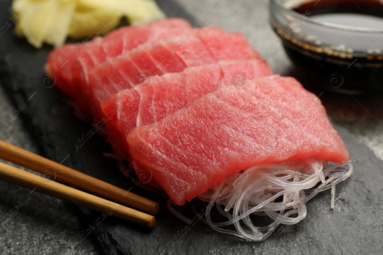 Photo of Tasty sashimi (pieces of fresh raw tuna), glass noodles and chopsticks on black board, closeup