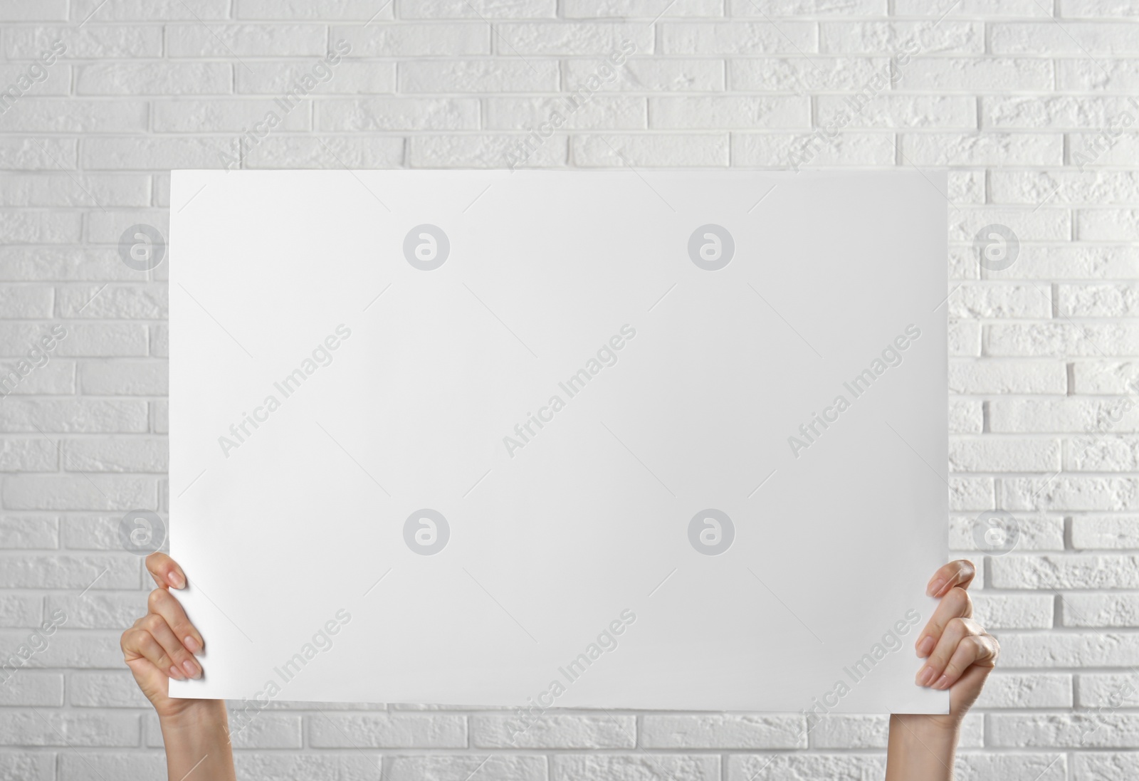 Photo of Woman holding blank poster near white brick wall, closeup. Mockup for design