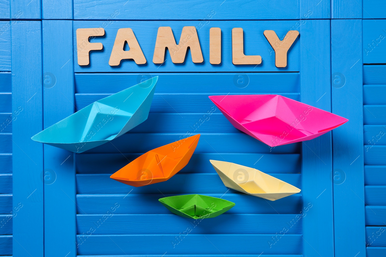 Photo of Paper ships and word Family on blue wooden background, flat lay