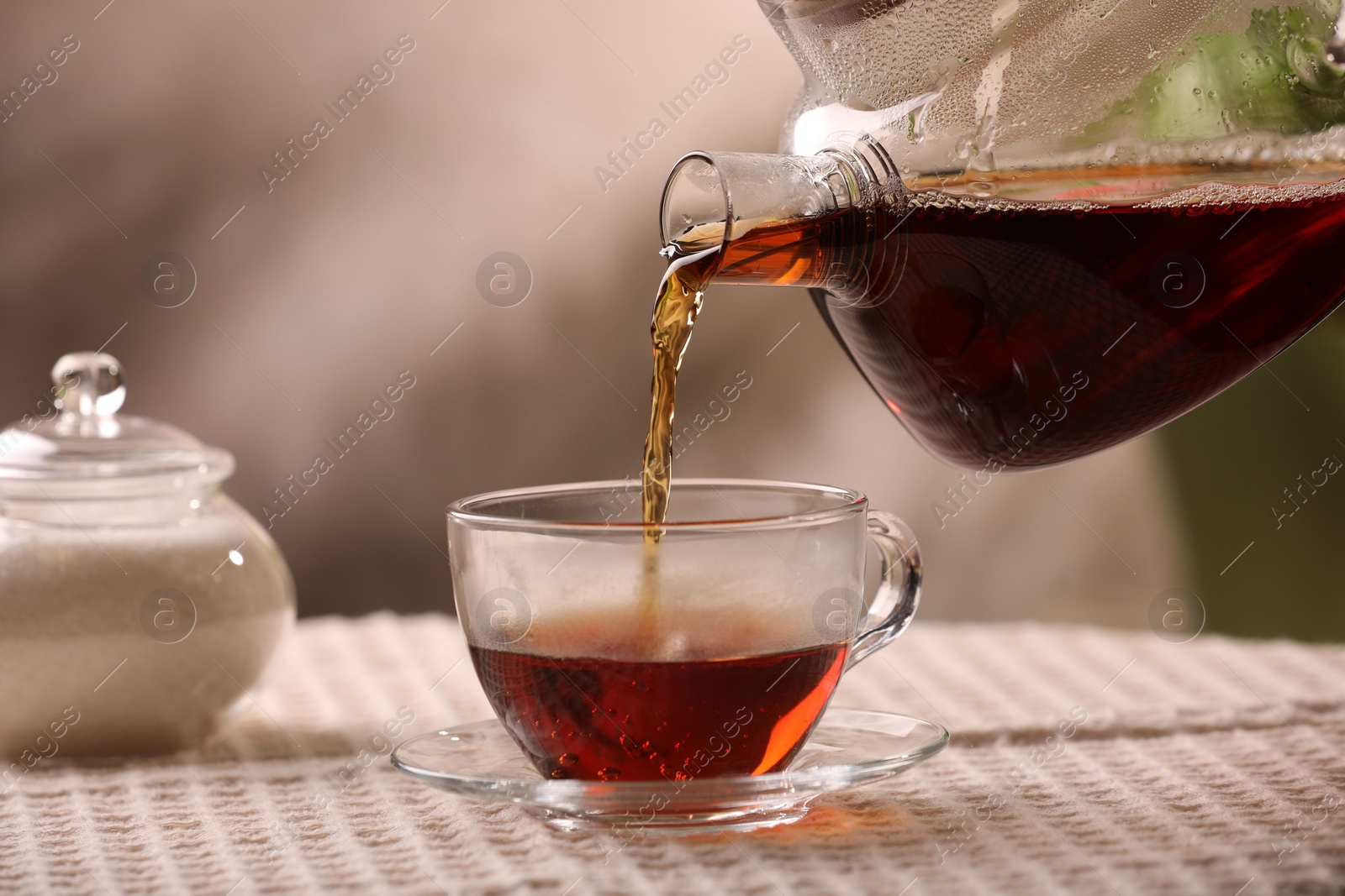 Photo of Pouring aromatic tea into cup at table, closeup