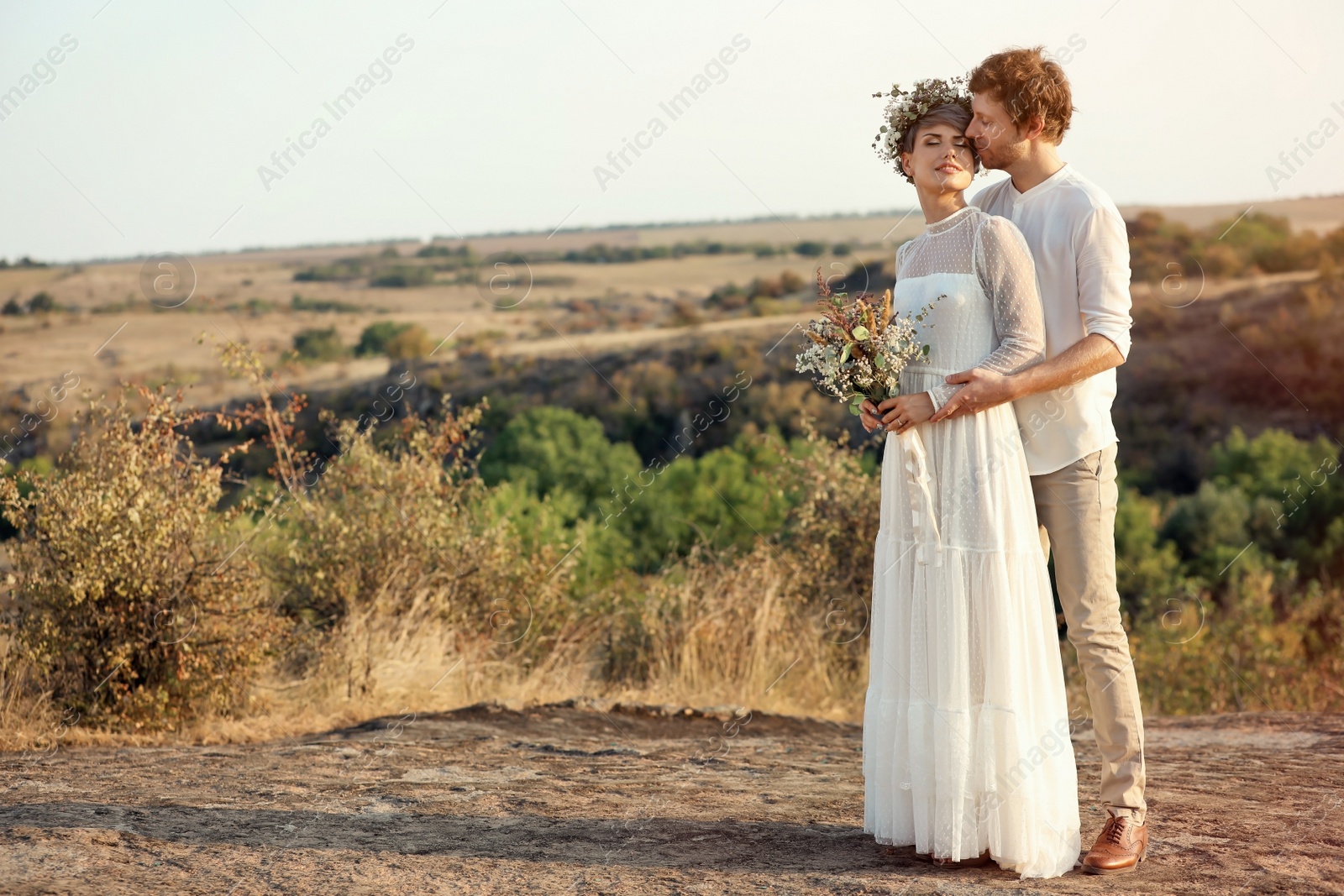 Photo of Happy newlyweds with beautiful field bouquet outdoors