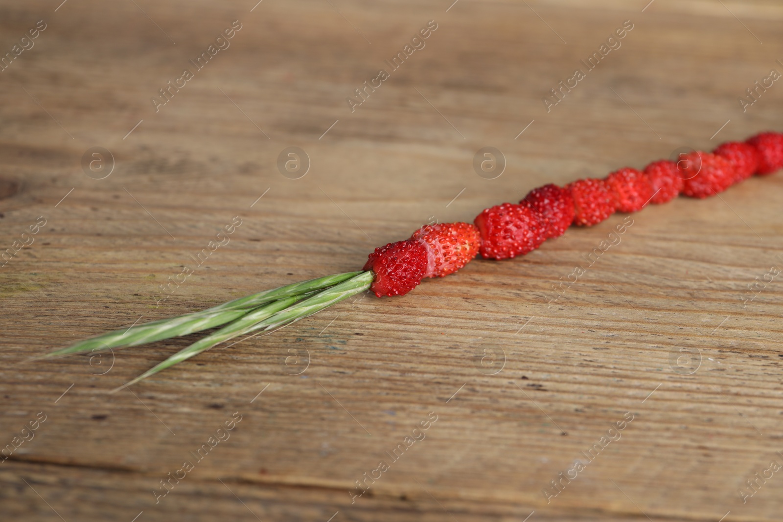 Photo of Grass stem with wild strawberries on wooden table, closeup