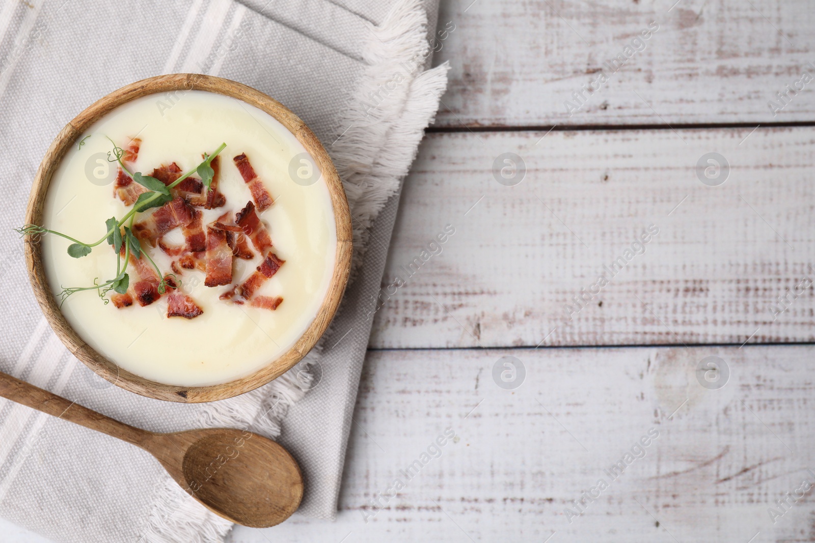 Photo of Delicious potato soup with bacon and microgreens in bowl served on wooden table, flat lay. Space for text