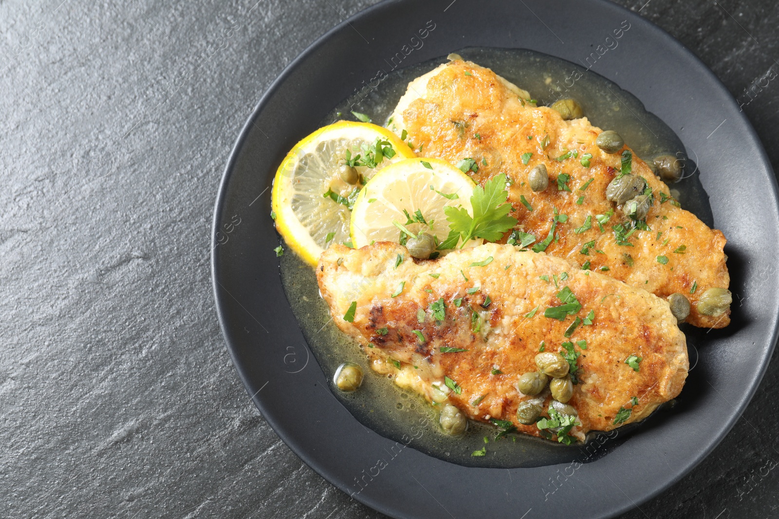 Photo of Delicious chicken piccata on black table, top view