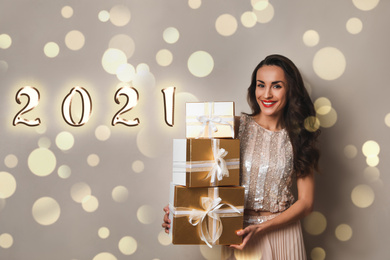 Beautiful woman with gift boxes on beige background. Christmas celebration