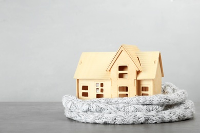 Photo of Wooden house model and scarf on light grey table. Heating efficiency