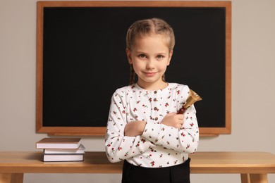 Photo of Pupil with school bell near desk and chalkboard in classroom