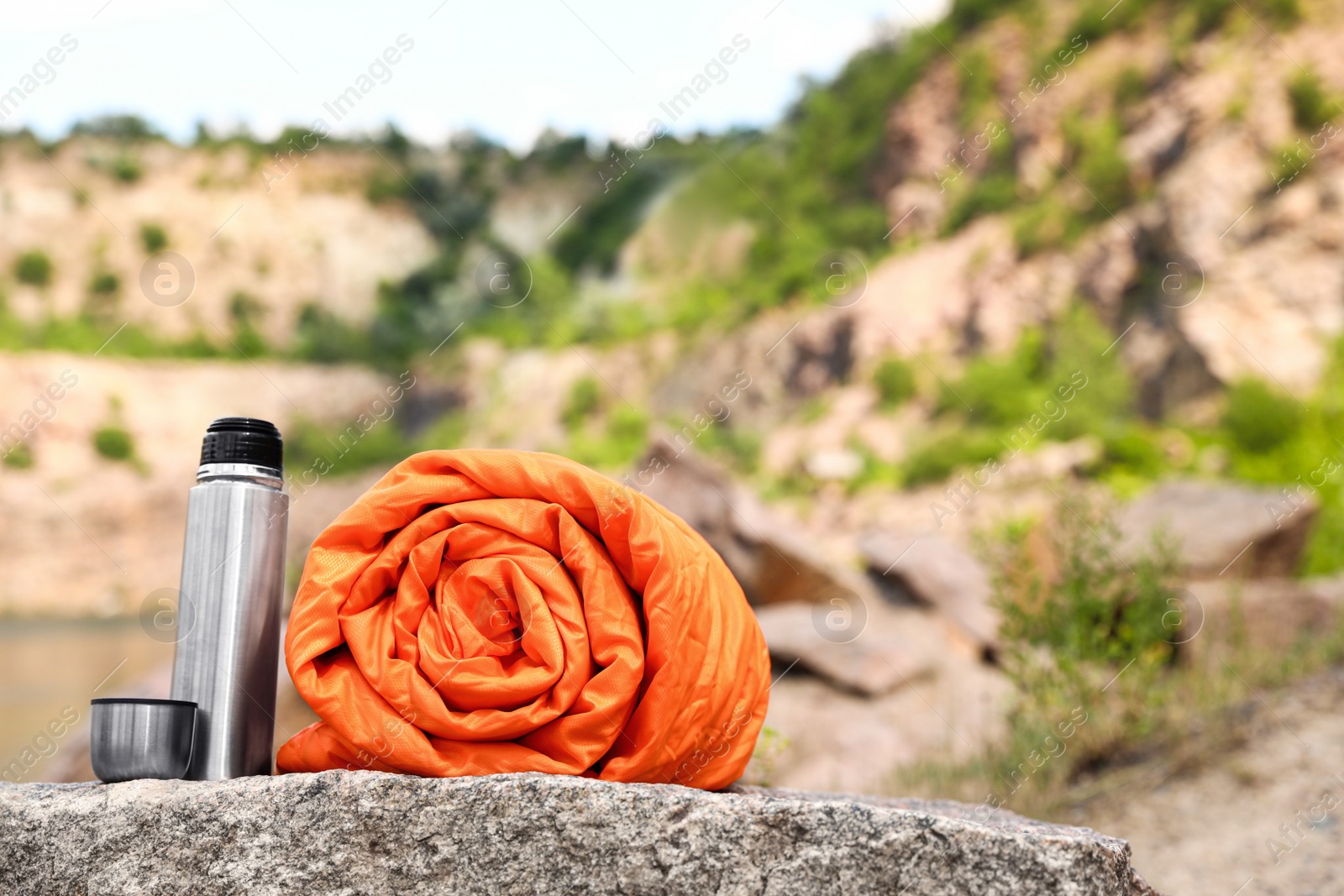 Photo of Sleeping bag and thermos outdoors on sunny day. Space for text