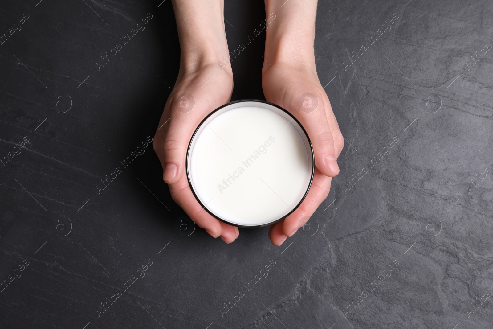 Photo of Woman holding glass of milk at black table, top view