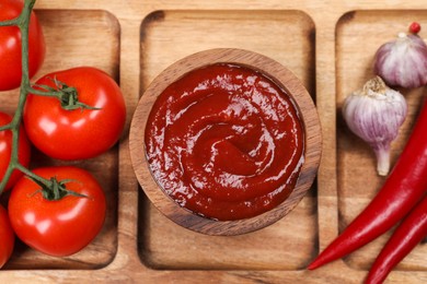 Photo of Delicious ketchup in bowl and products on wooden plate, top view. Tomato sauce