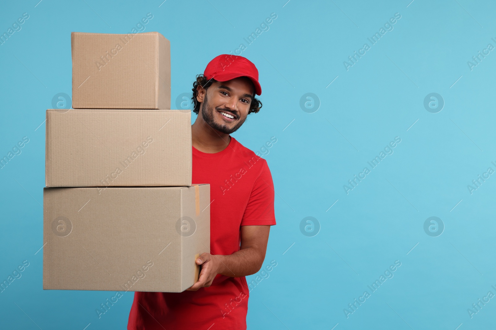 Photo of Happy courier with parcels on light blue background, space for text