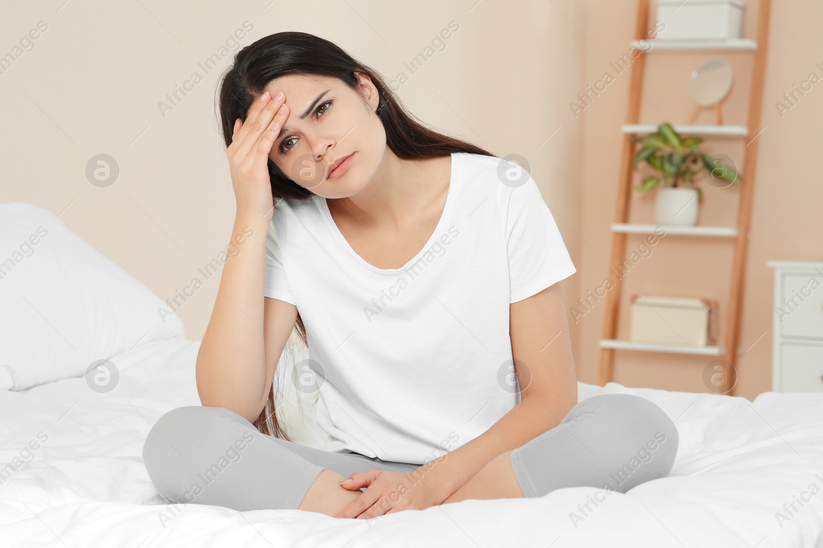 Photo of Young woman suffering from headache on bed at home. Hormonal disorders