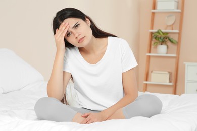 Photo of Young woman suffering from headache on bed at home. Hormonal disorders