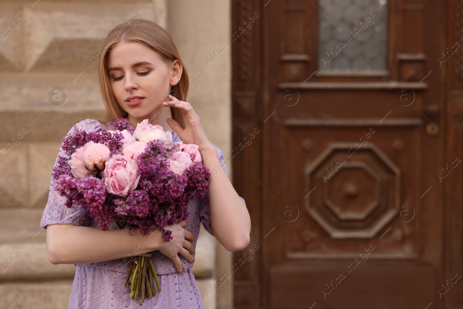 Photo of Beautiful woman with bouquet of spring flowers near building outdoors, space for text