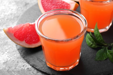 Tasty freshly made grapefruit juice and fruit on grey table