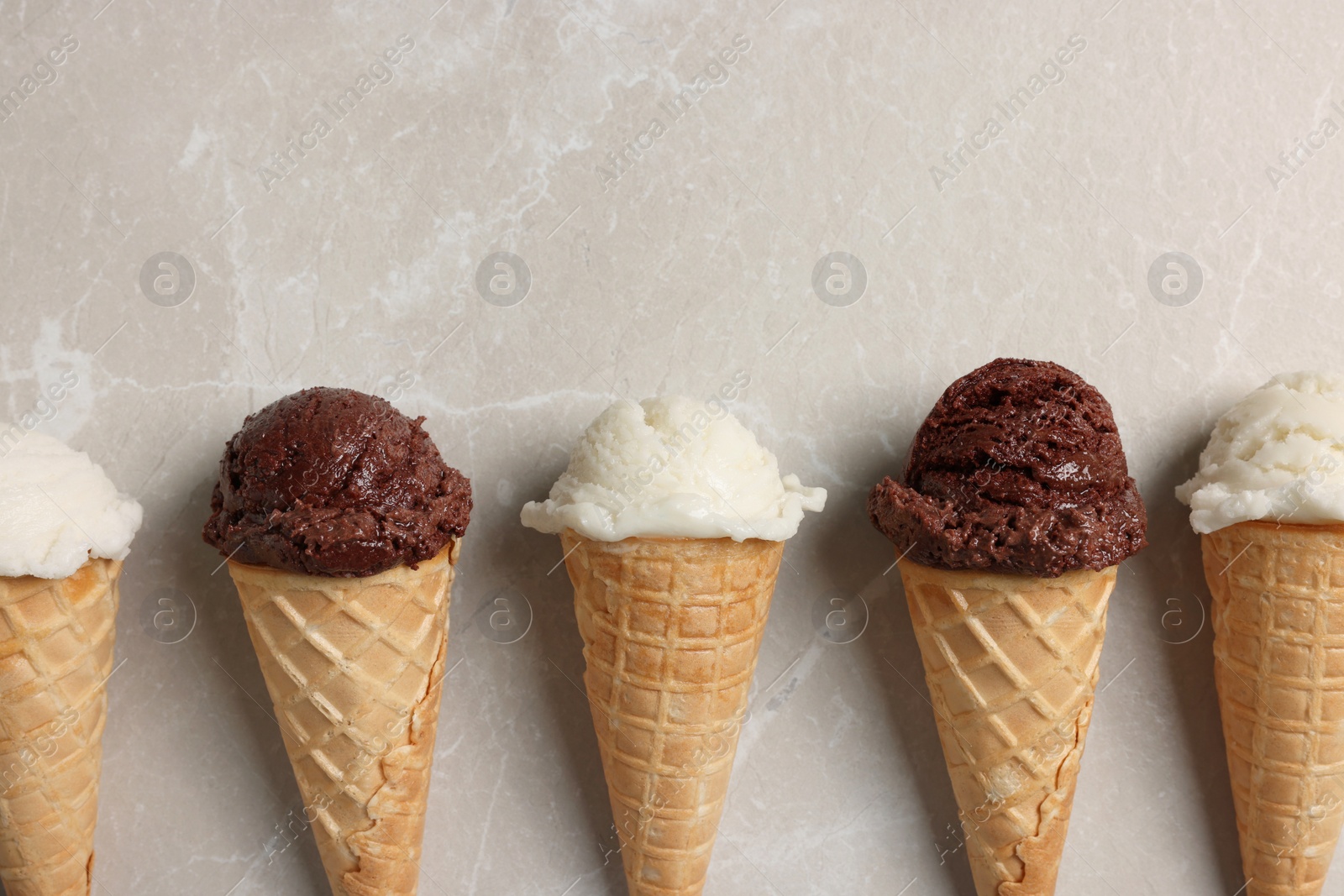 Photo of Tasty ice cream scoops in waffle cones on light marble table, flat lay. Space for text