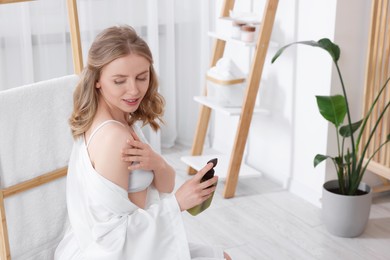 Beautiful young woman applying oil onto shoulder indoors