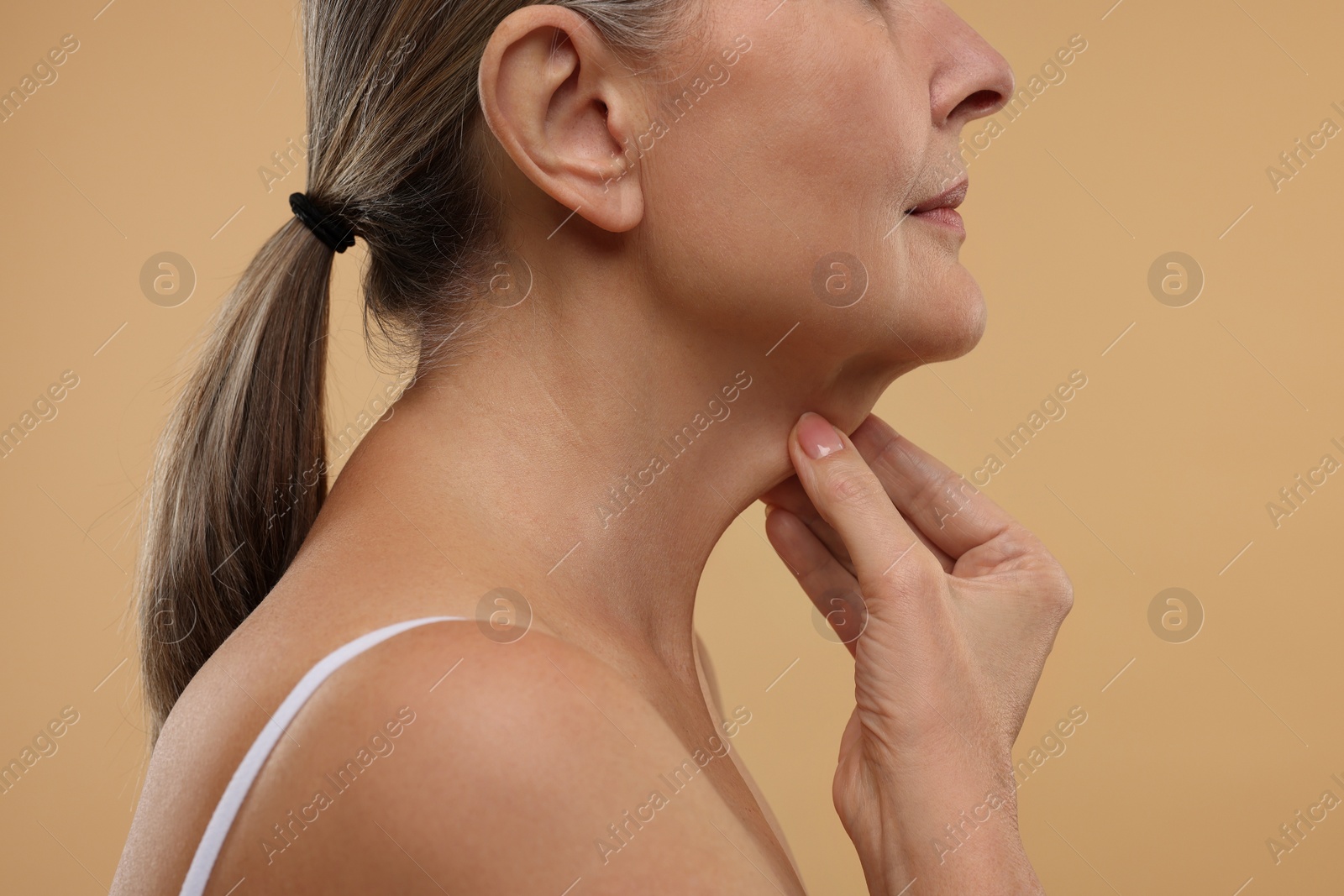 Photo of Mature woman touching her neck on beige background, closeup