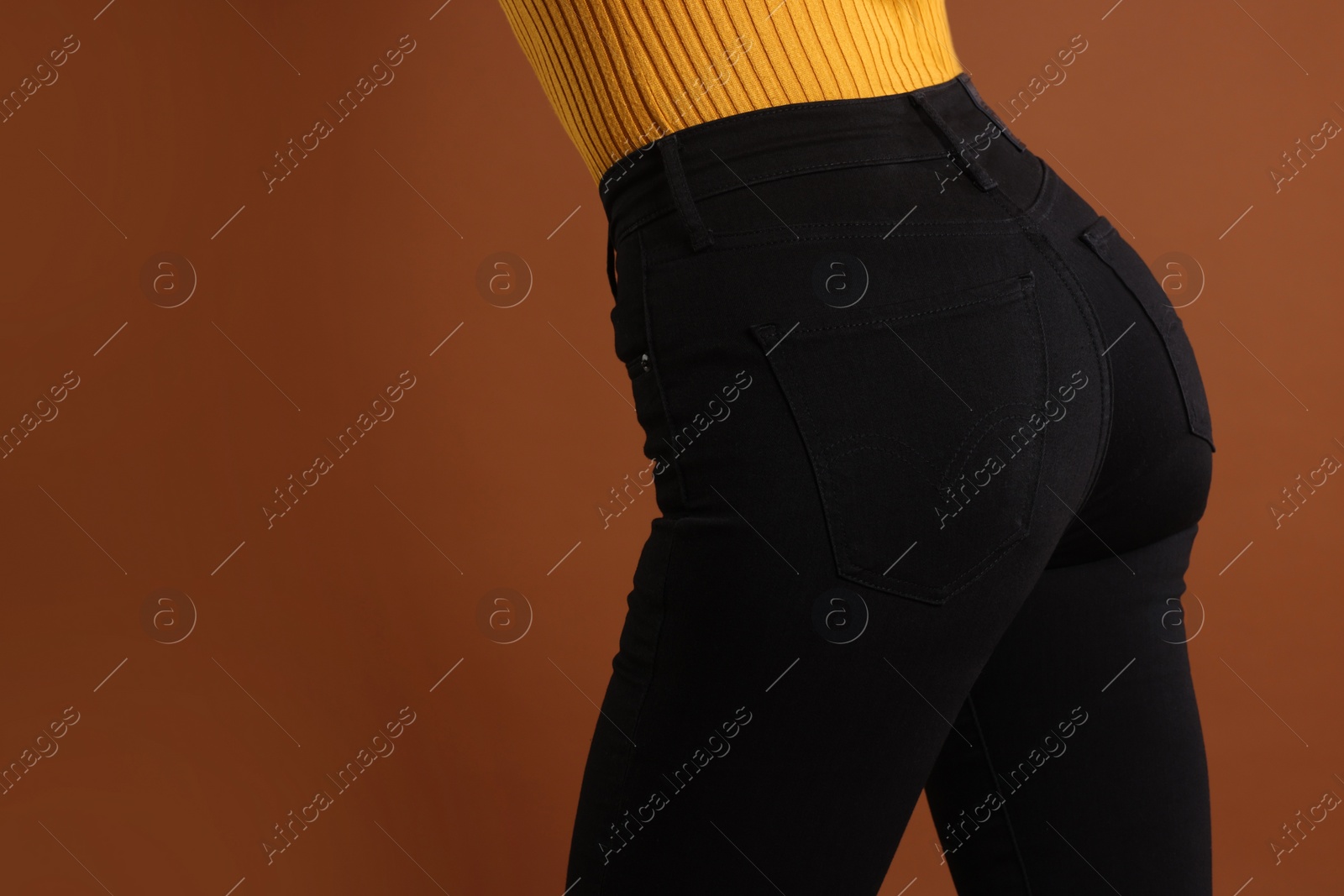 Photo of Woman wearing stylish black jeans on brown background, closeup. Space for text