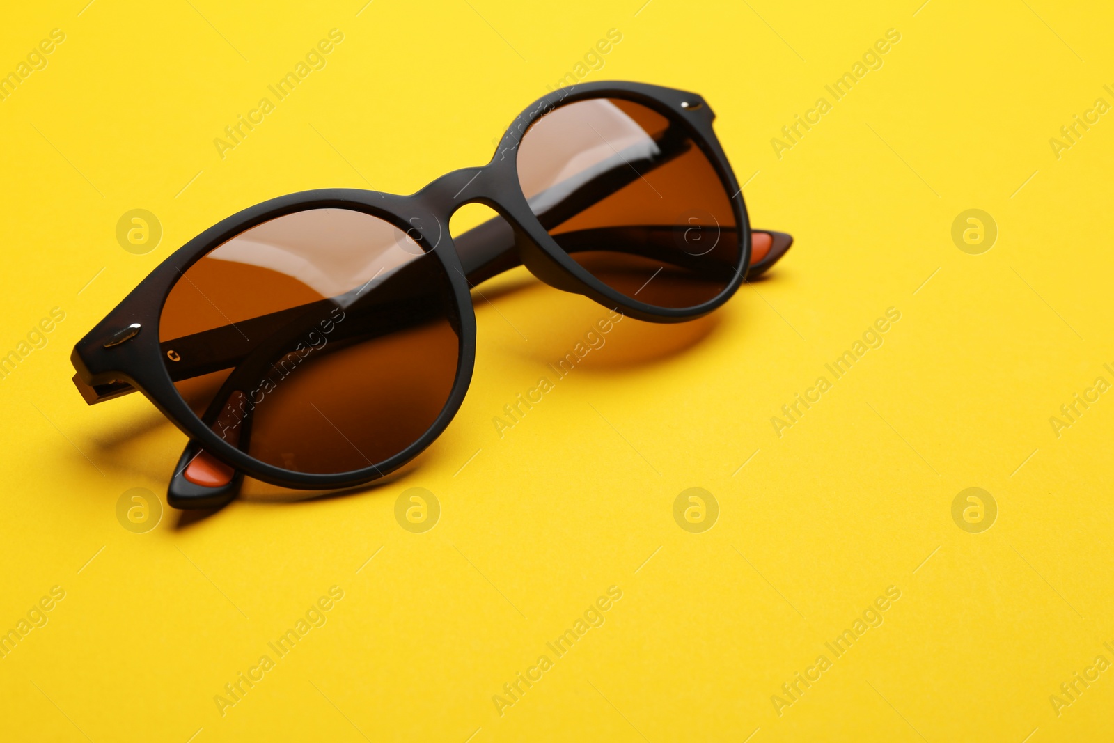 Photo of Stylish sunglasses on yellow background. Fashionable accessory