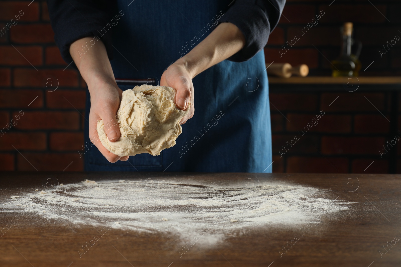 Photo of Making bread. Woman kneading dough at wooden table in kitchen, closeup