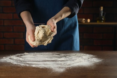 Photo of Making bread. Woman kneading dough at wooden table in kitchen, closeup