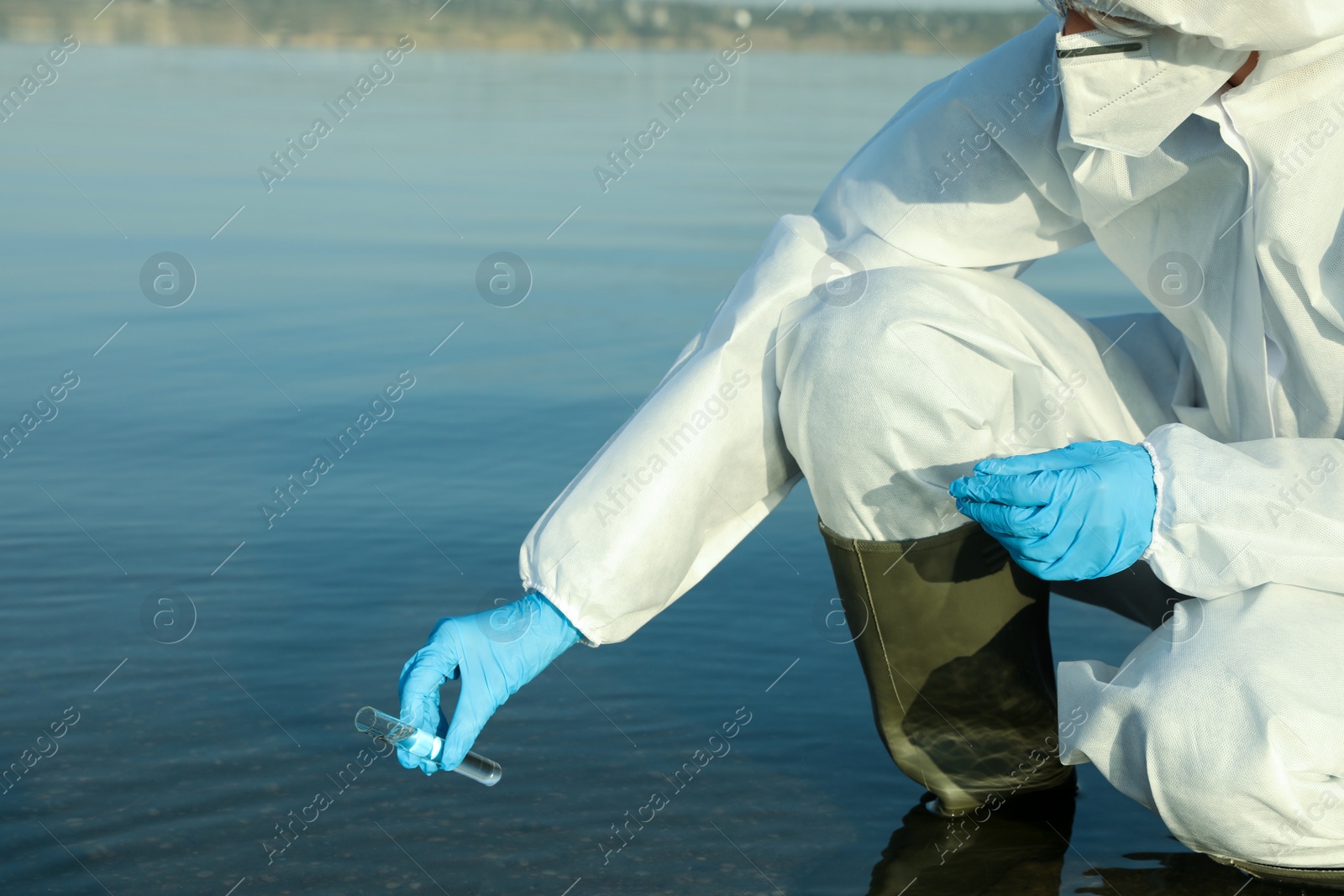 Photo of Scientist in chemical protective suit with test tube taking sample from river for analysis, closeup