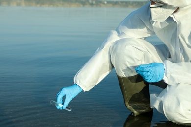 Photo of Scientist in chemical protective suit with test tube taking sample from river for analysis, closeup