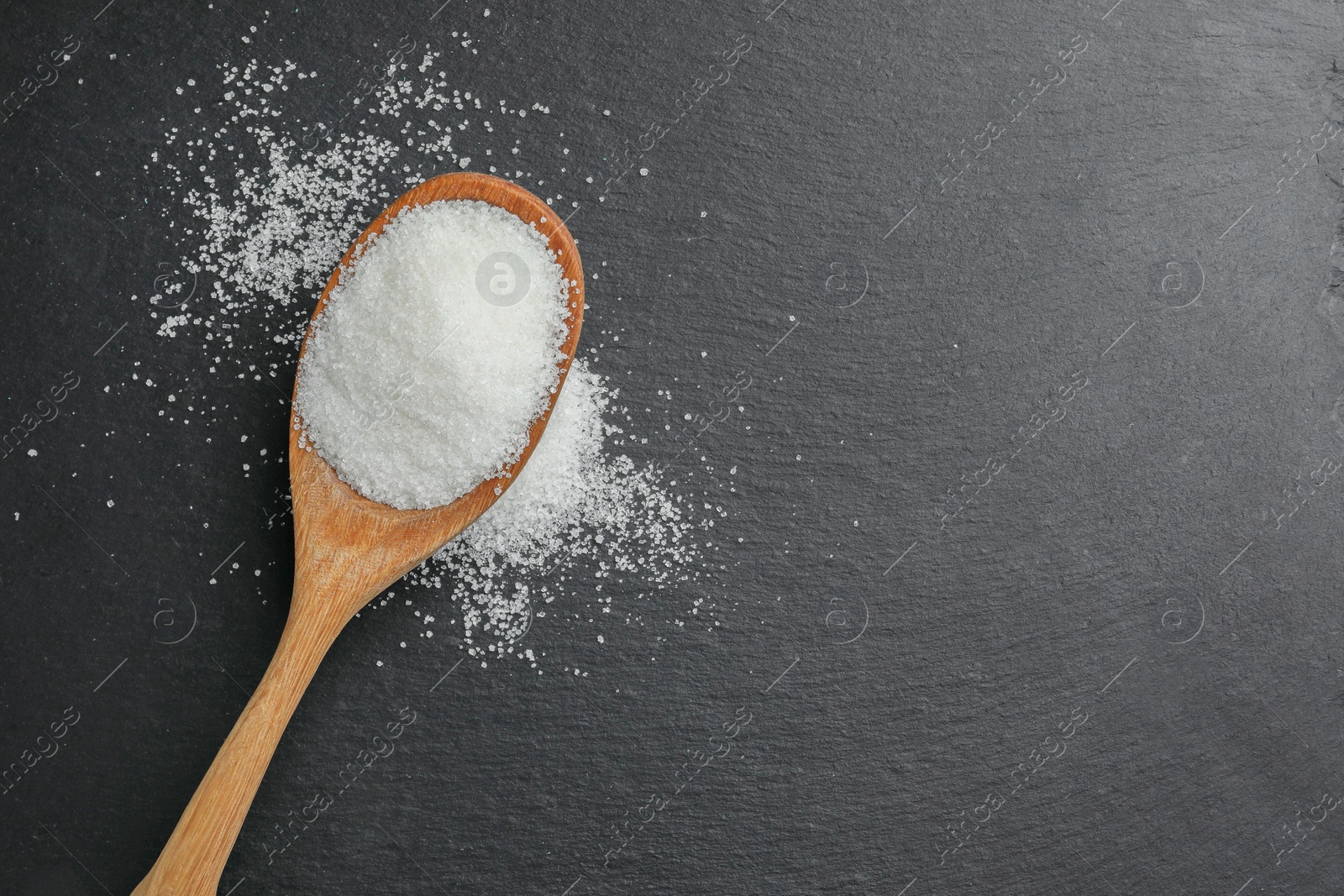 Photo of Spoon with granulated sugar on black table, top view. Space for text