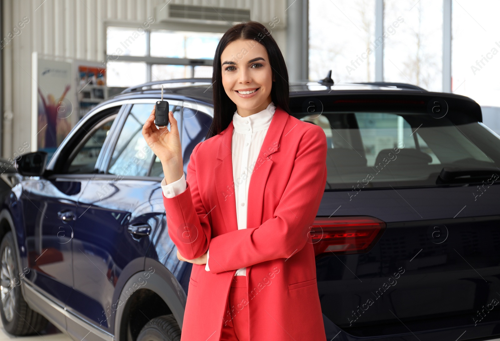 Photo of Saleswoman with key near car in dealership