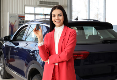 Photo of Saleswoman with key near car in dealership